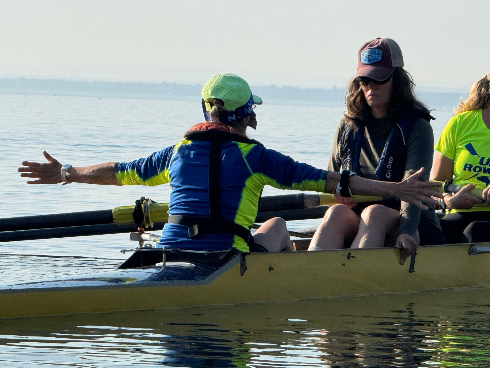Coxswain in a boat has arms out wide as they direct the rowing shell. 