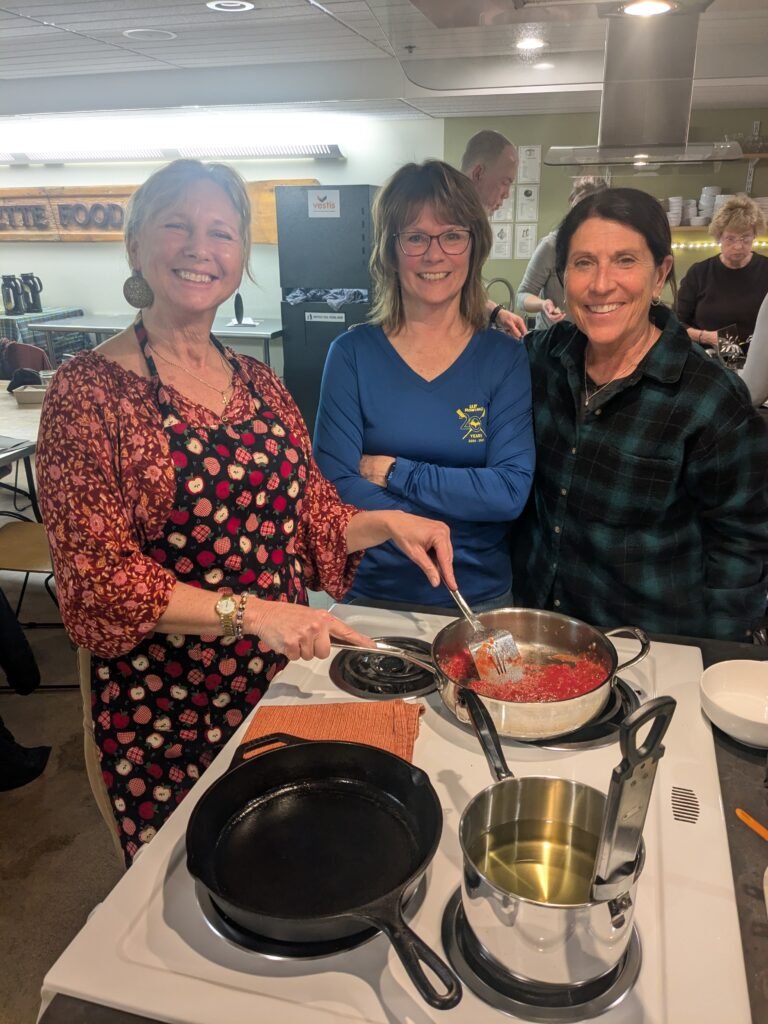 Rowers stirring a sauce and smiling during an Indian cooking class at the Marquette Food Co-op. 